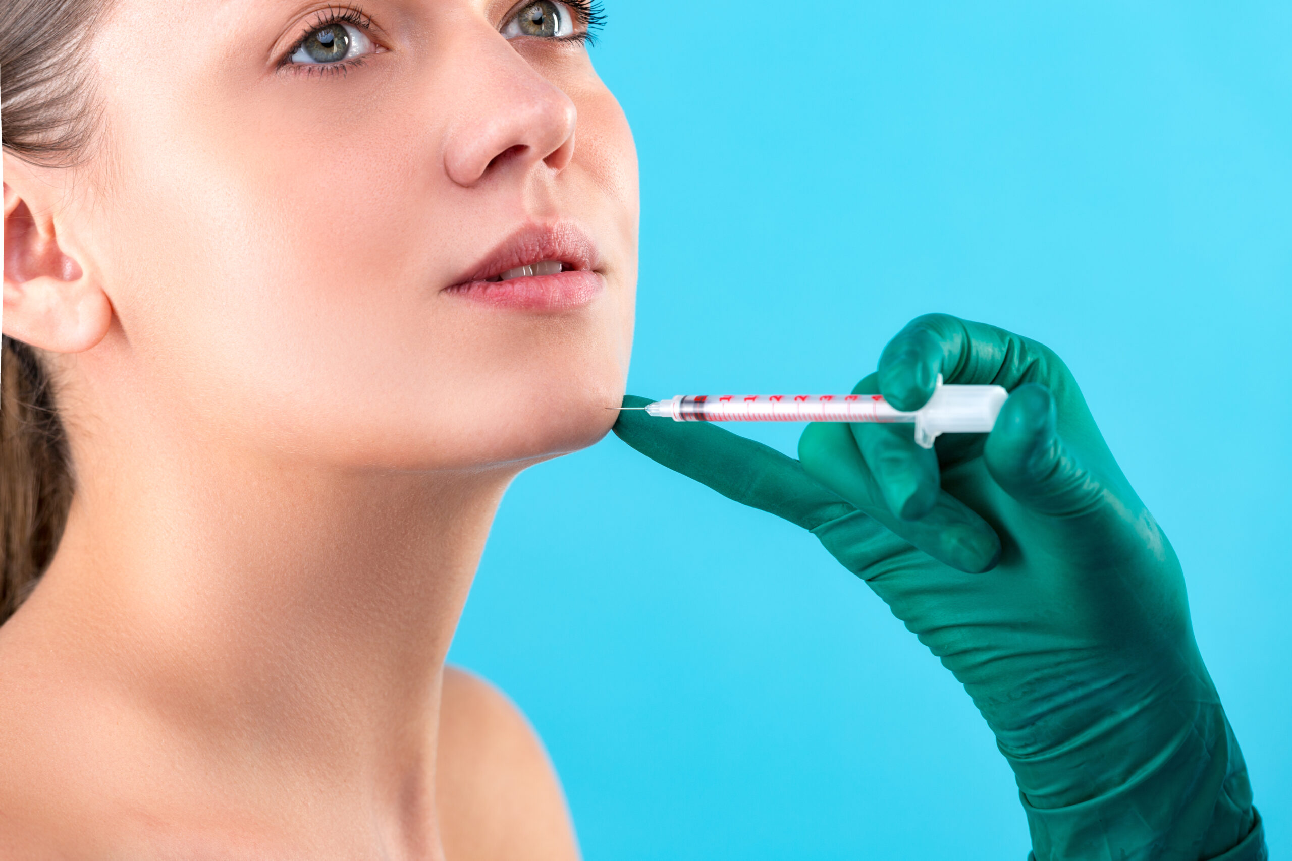 Beautiful woman face and beautician hands with syringe. Doctor makes cosmetic injection. Clean Beauty concept.